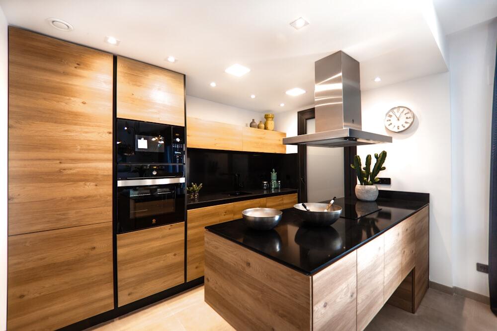Dapur oak dengan kolom hitam, meja hitam, dan cooker hood