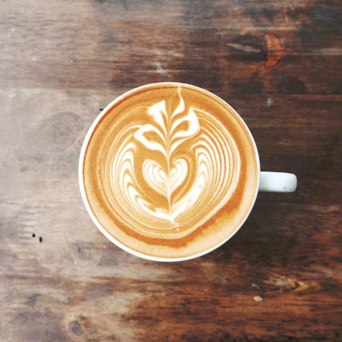 Secangkir kopi dengan latte art di atas meja kayu